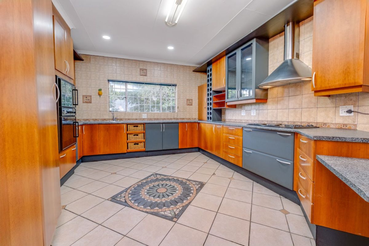 Spacious kitchen featuring wood-tone and grey cabinetry, built-in oven, stainless steel extractor fan, tiled splashbacks, and decorative floor tiling.