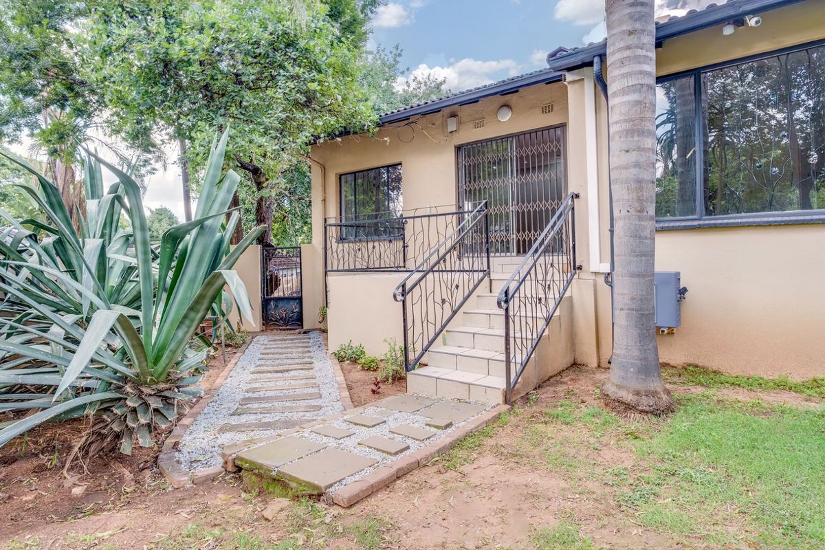 Rear exterior view featuring a raised patio entrance with metal security gate, tiled steps, and a stone-paved garden pathway.