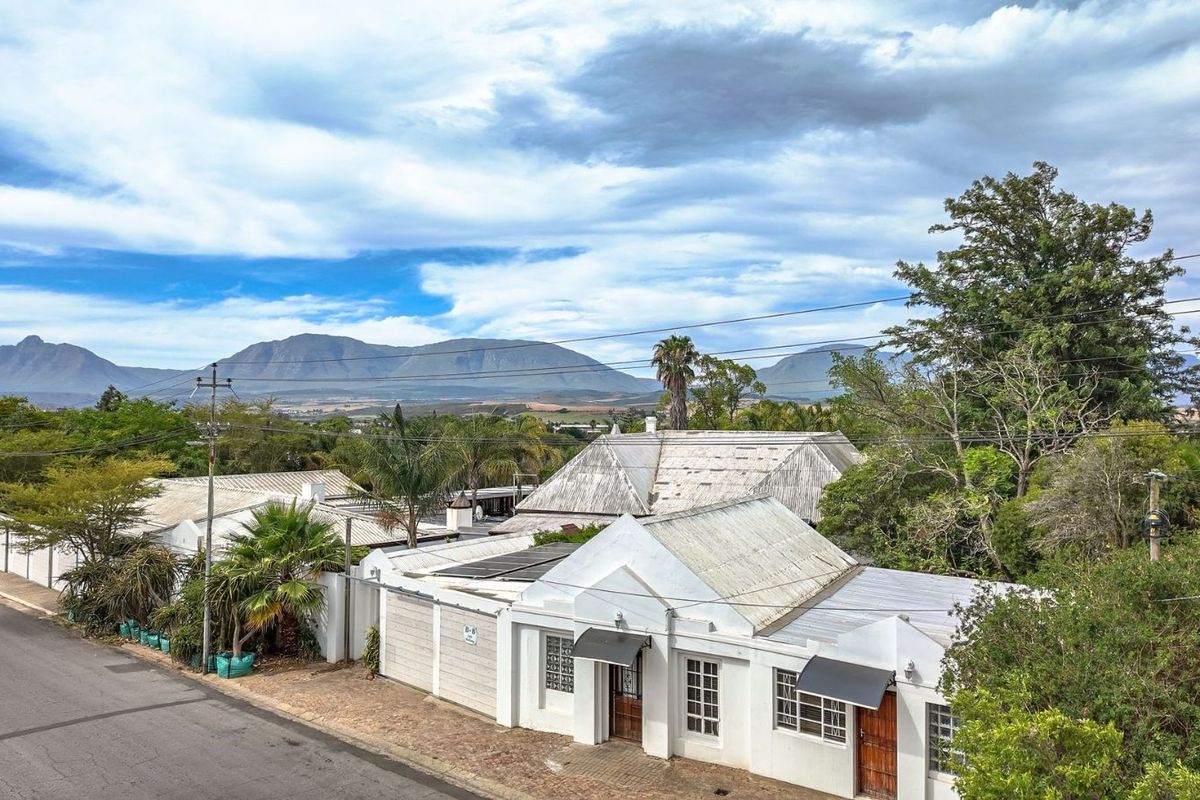 An elevated view of the guest house property, showcasing the white exterior facade, pitched roof structure, and surrounding landscaped grounds with mountain views.