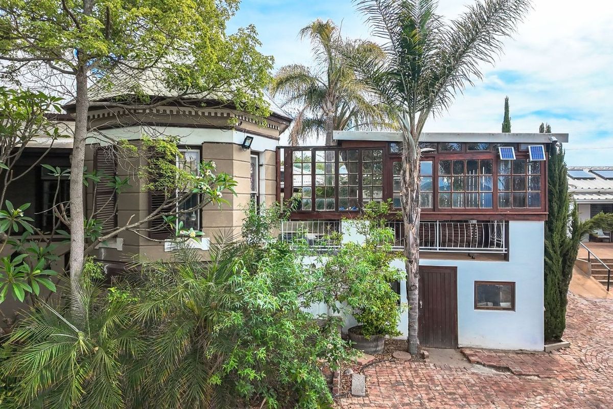 Exterior view of the guest house featuring a mix of traditional architecture, a raised timber-framed balcony, and established garden landscaping with brick paving.