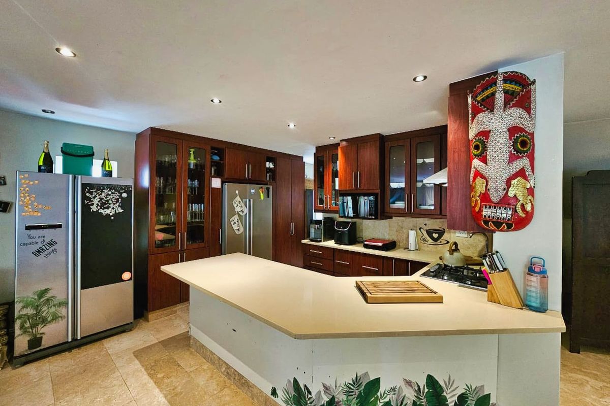 A functional kitchen featuring dark wood cabinetry, a central breakfast bar with stone countertops, recessed lighting, and tiled flooring.