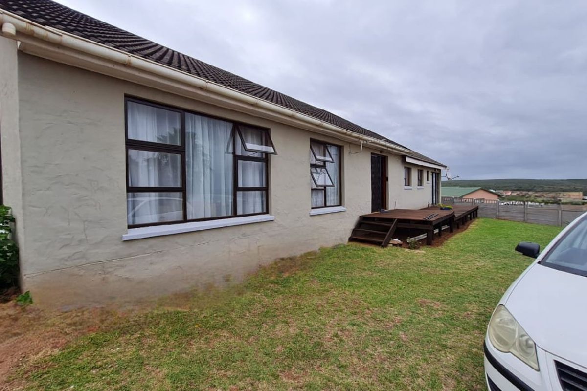 Rear view of the house featuring a raised timber deck, tiled roof, and aluminium-framed windows overlooking a grassed garden area.