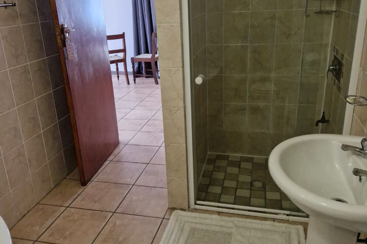 A functional bathroom featuring a glass-enclosed shower, pedestal basin, and tiled flooring, with direct access to an adjacent room.