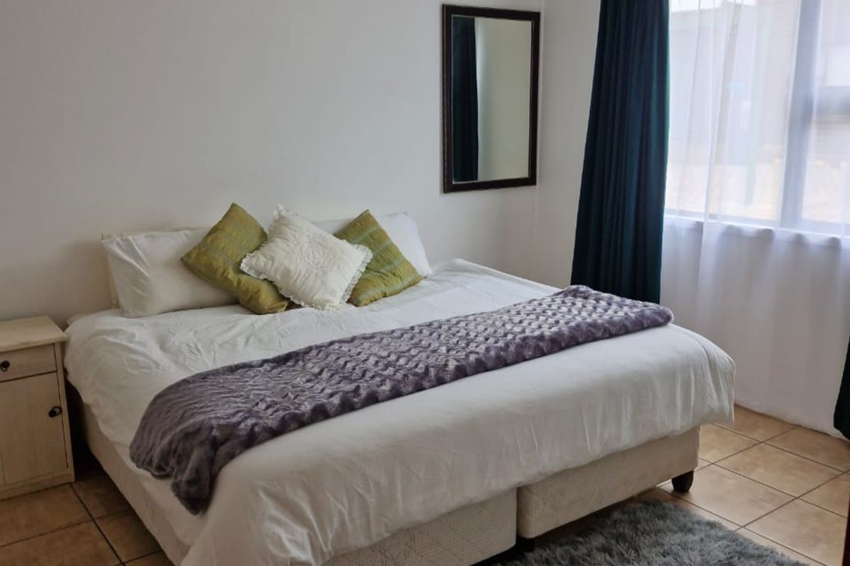 A well-lit bedroom featuring neutral tiled flooring, a large window with curtains, and a simple, functional layout.