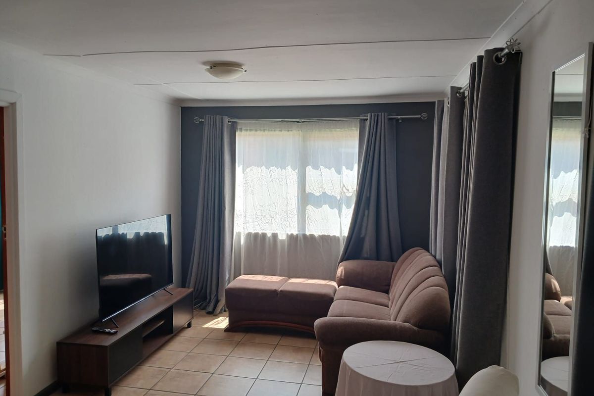 A functional living room featuring tiled flooring, a dark accent wall, and large windows with curtain tracks.