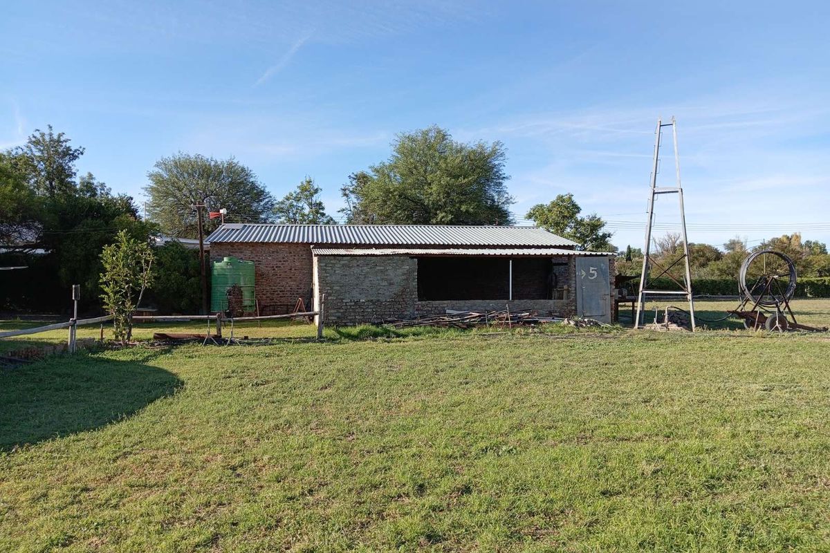 A detached outbuilding or utility structure featuring exposed brickwork, a corrugated metal roof, and an adjacent water tank on a large grassed plot.