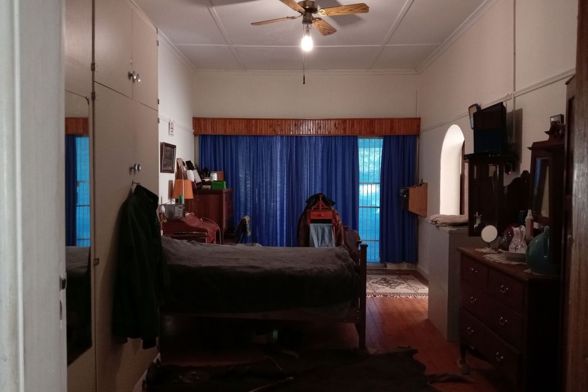 A spacious bedroom featuring built-in cabinetry, wooden flooring, and a ceiling fan, with direct access to an outdoor area through large curtains.