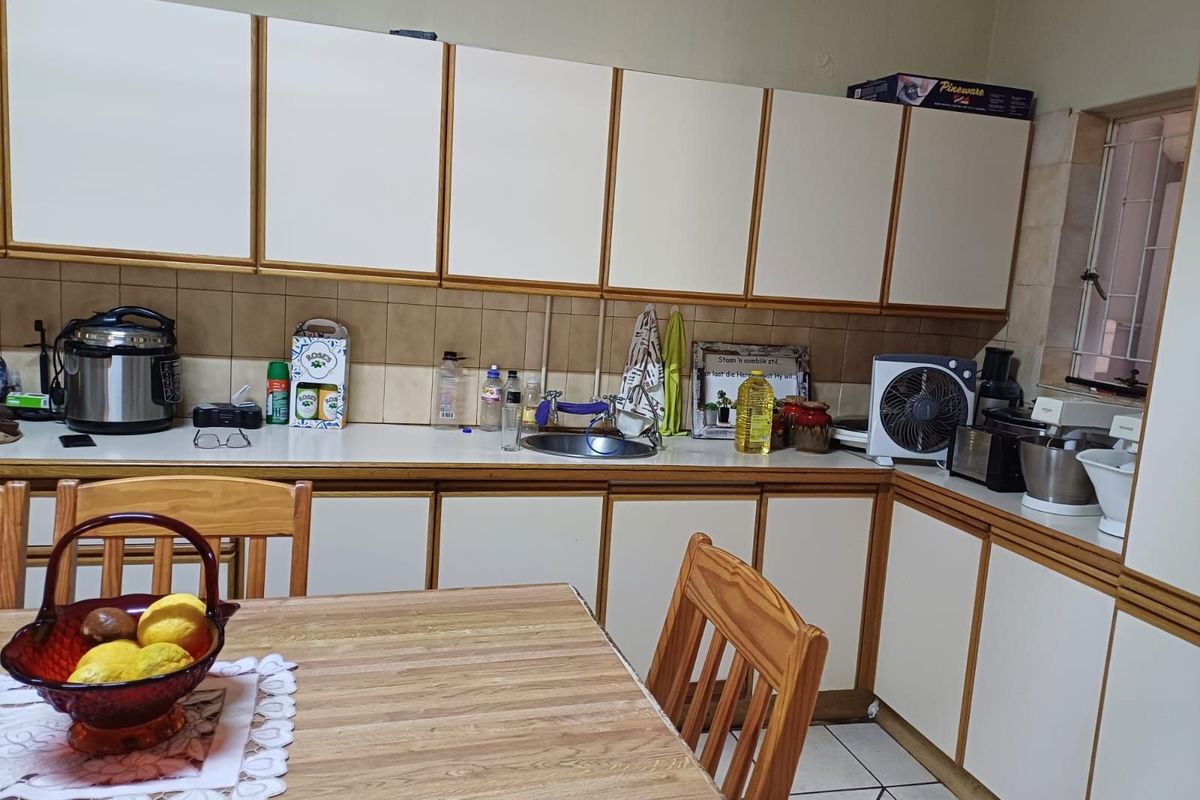 A functional kitchen featuring white cabinetry with wood trim, tiled backsplash, and a stainless steel sink, offering a classic layout with ample storage space.