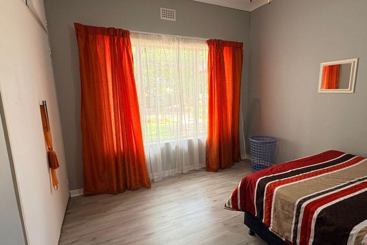 A bedroom featuring light-toned laminate flooring, built-in cupboards, and a large window with curtains.