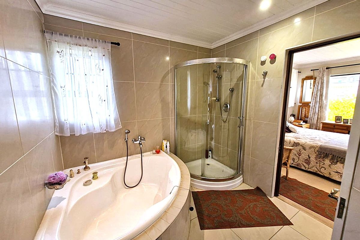 A functional bathroom featuring a corner bathtub, a separate glass-enclosed shower, and neutral wall tiling, with direct access to an adjacent bedroom.