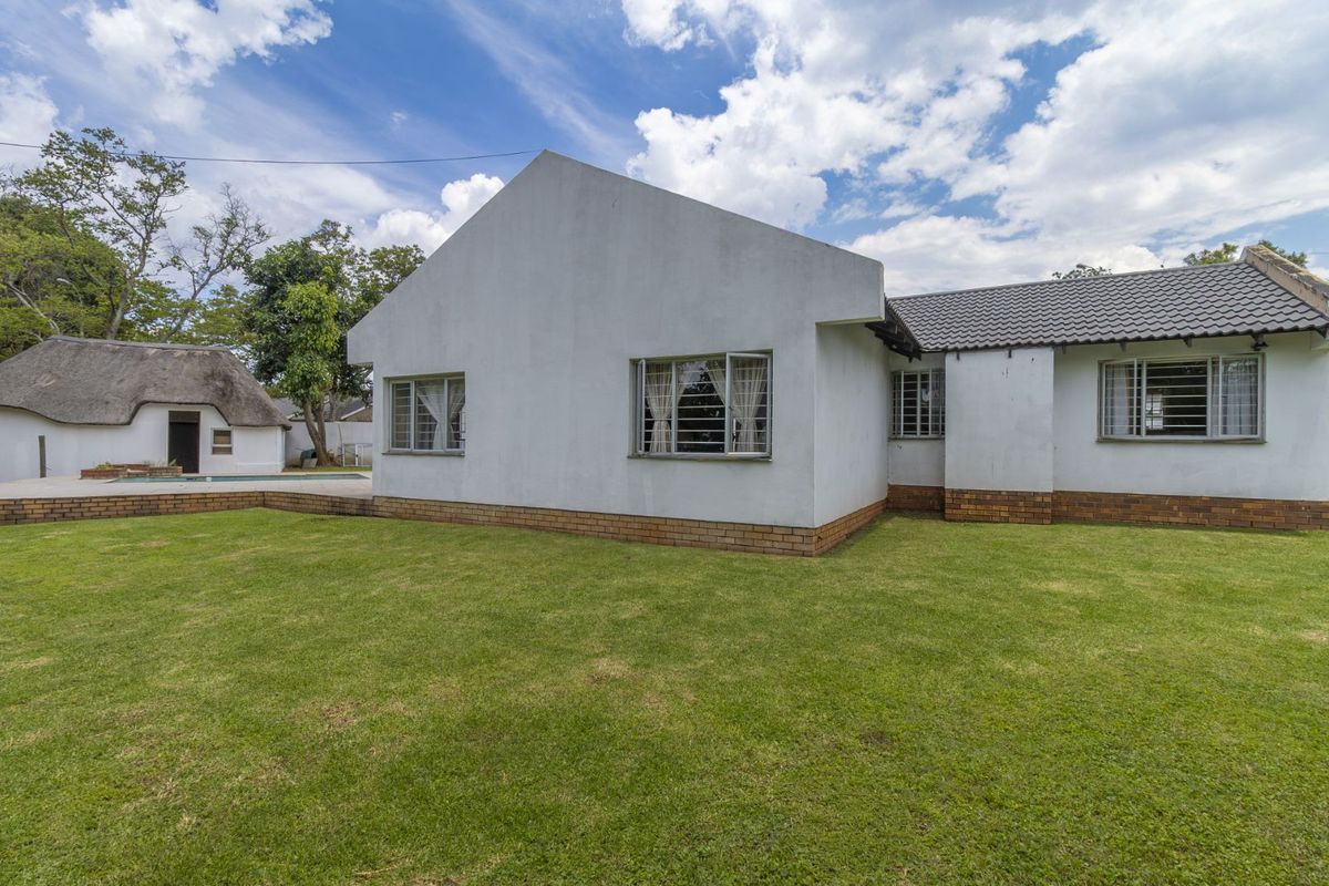 Rear view of the house featuring a white plastered facade, tiled roof, and metal window frames, overlooking a spacious green lawn.