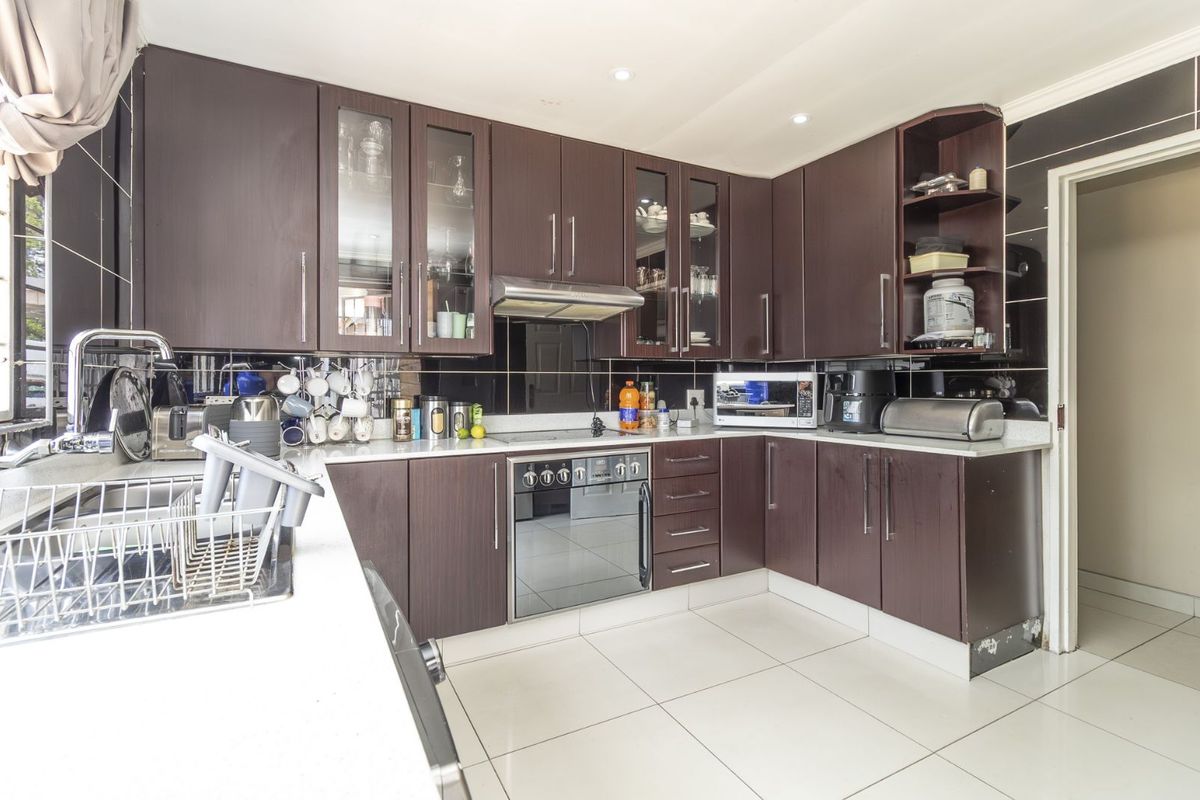 A functional kitchen featuring dark wood cabinetry, stone countertops, a built-in oven, extractor fan, and tiled flooring.