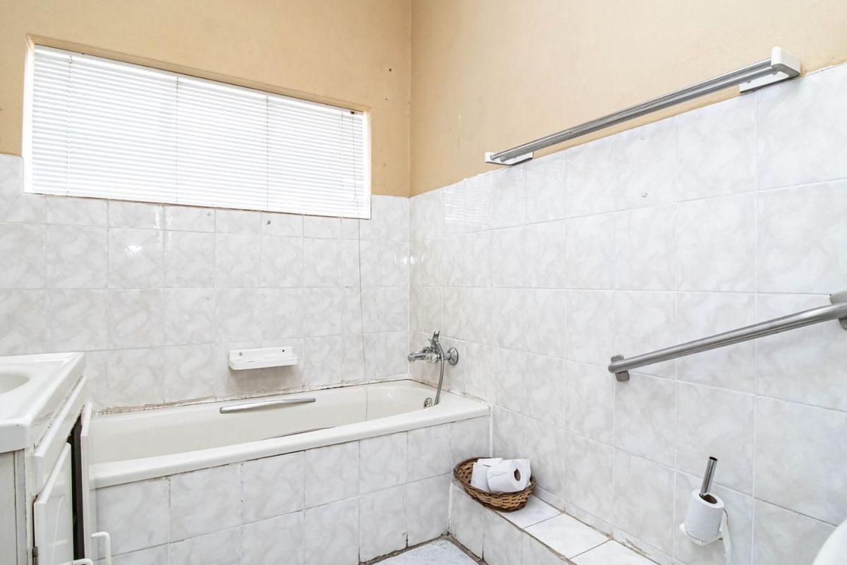 A functional bathroom featuring a built-in bathtub, wall-mounted grab rails, and a vanity basin with tiled wall finishes.