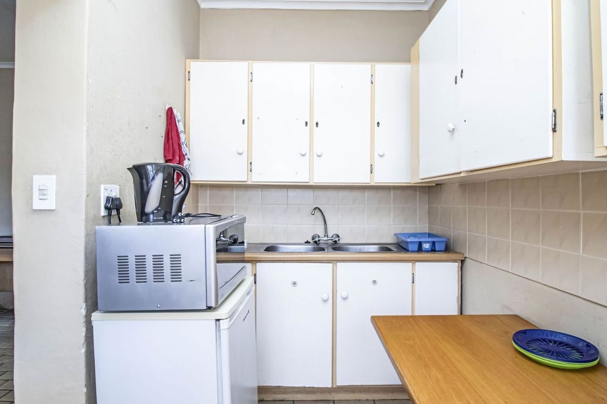 A compact kitchenette featuring white laminate cabinetry, a double stainless steel sink, and tiled backsplash, suitable for a small office or utility space.