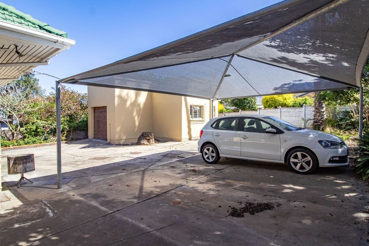 Exterior view of a paved driveway area featuring a shade cloth carport structure and a detached garage building.