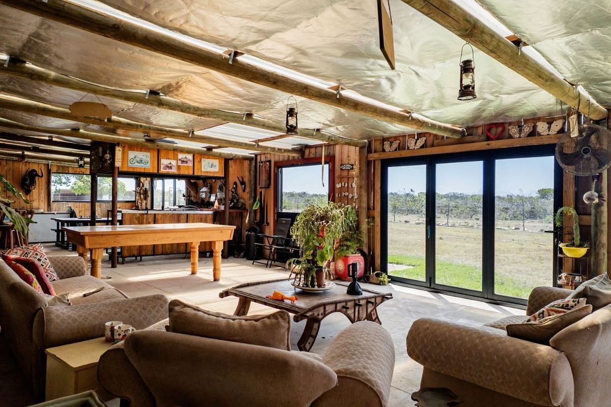 Spacious rustic entertainment area featuring timber walls, exposed beam ceiling with translucent roofing, and large folding glass doors opening to the landscape.