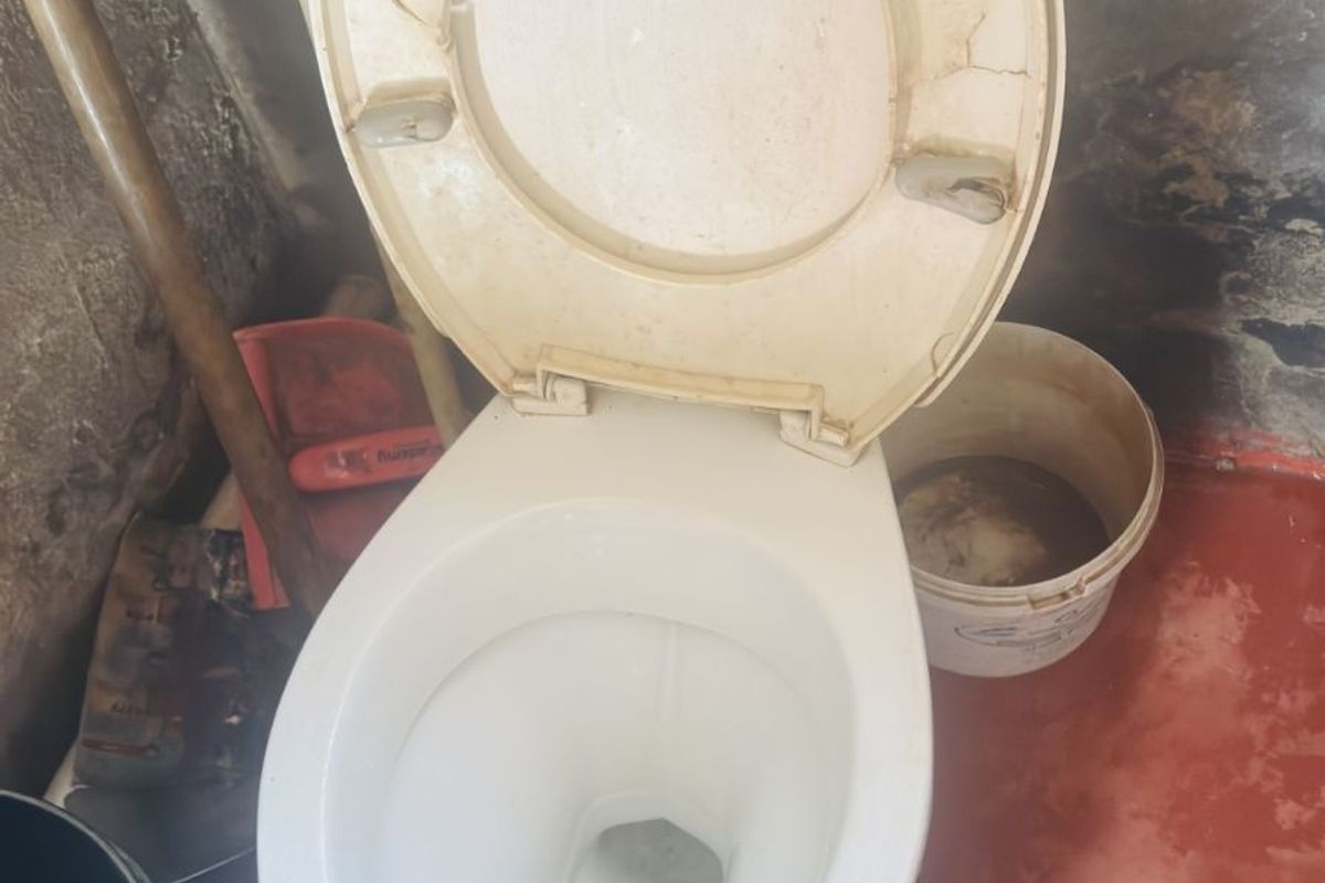 A bathroom featuring a standard toilet with a cracked seat and visible wear on the surrounding wall and floor finishes.