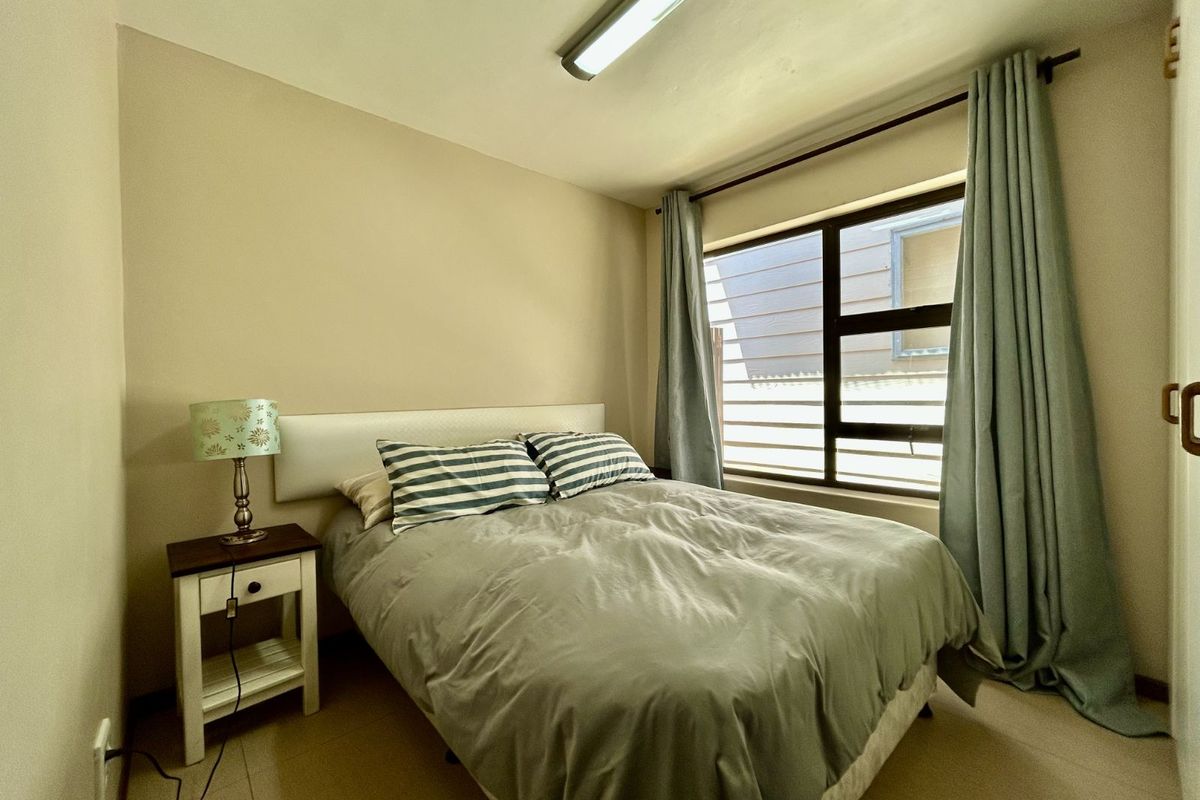 A compact bedroom featuring tiled flooring, a large window with curtain tracks, and a functional overhead light fixture.