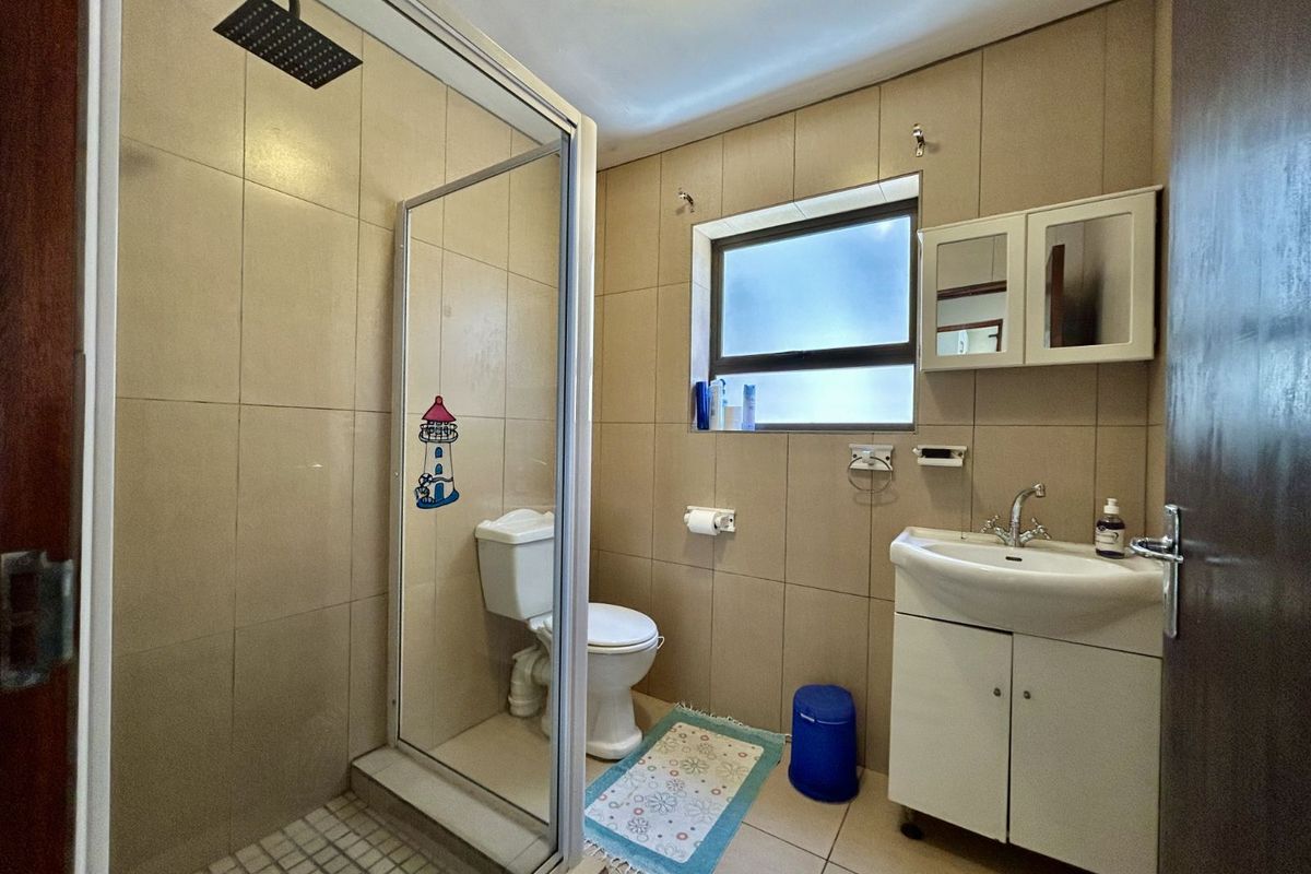 A functional bathroom featuring a glass-enclosed shower, pedestal vanity with storage, and neutral wall tiling.