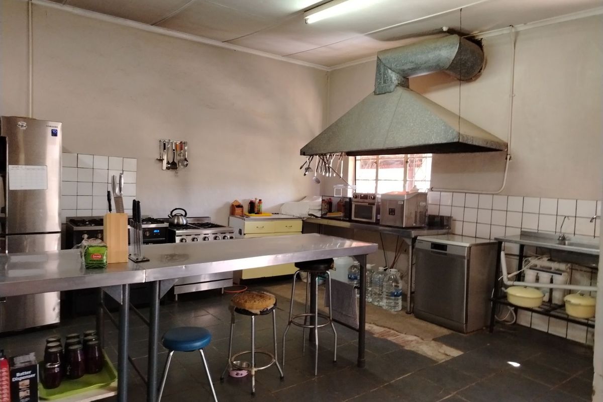 A functional commercial-style kitchen featuring stainless steel prep tables, a large industrial extractor hood, tiled splashbacks, and tiled flooring.