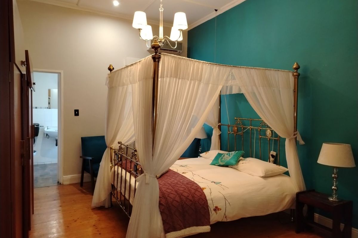A bedroom featuring polished timber flooring, a feature wall, and an en-suite bathroom access.