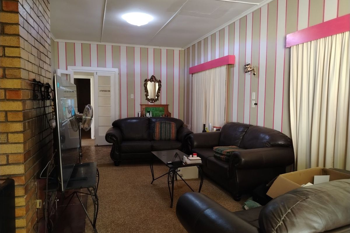 A living room featuring a brick fireplace, striped wallpaper, and carpeted flooring, providing a dated interior space with potential for modernization.