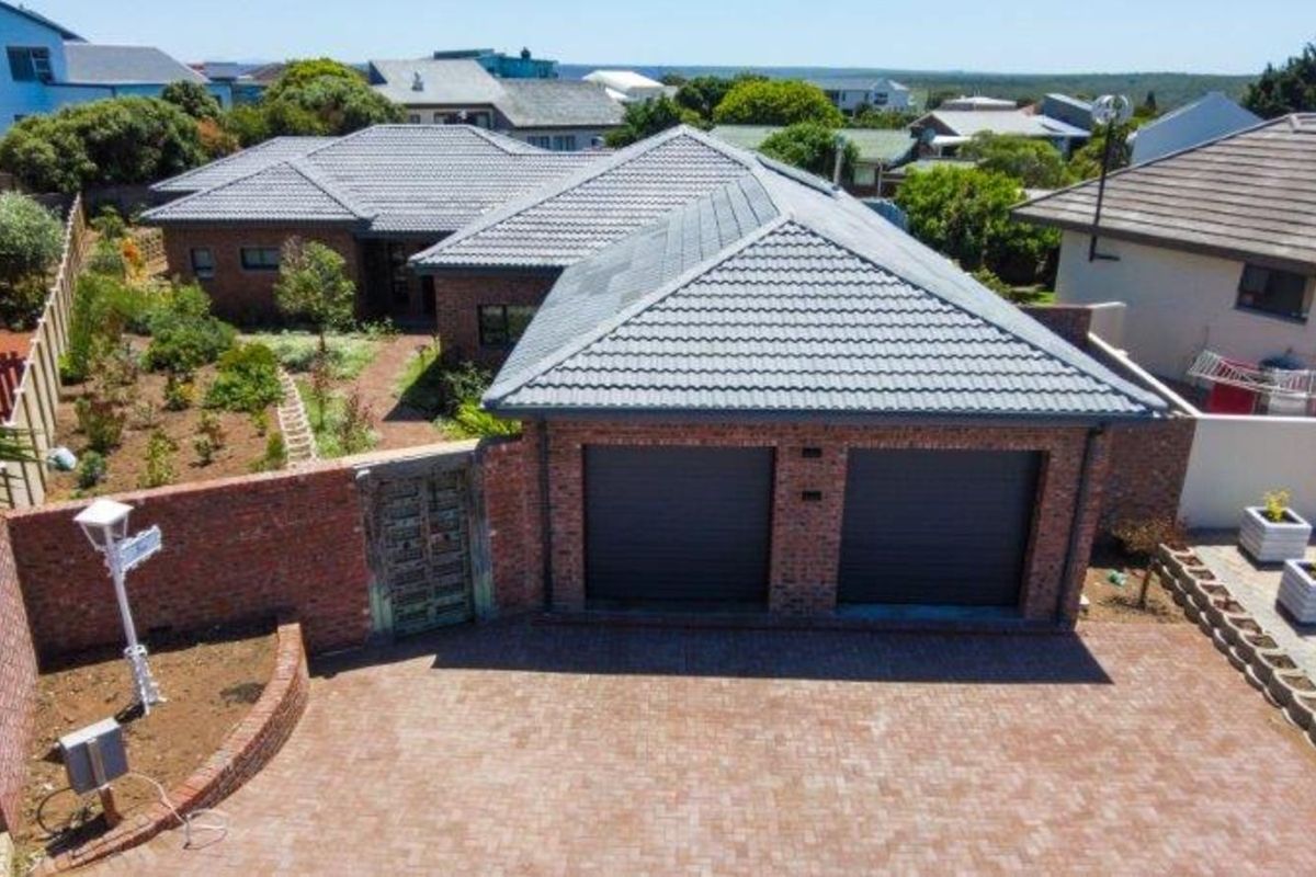 Aerial view of a brick-faced residential property featuring a double garage, paved driveway, and landscaped garden area.