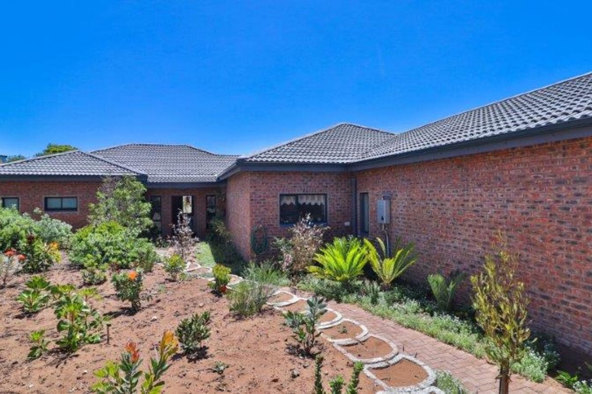 A view of the rear brick facade of the house, featuring a tiled roof and a landscaped garden with a paved pathway.