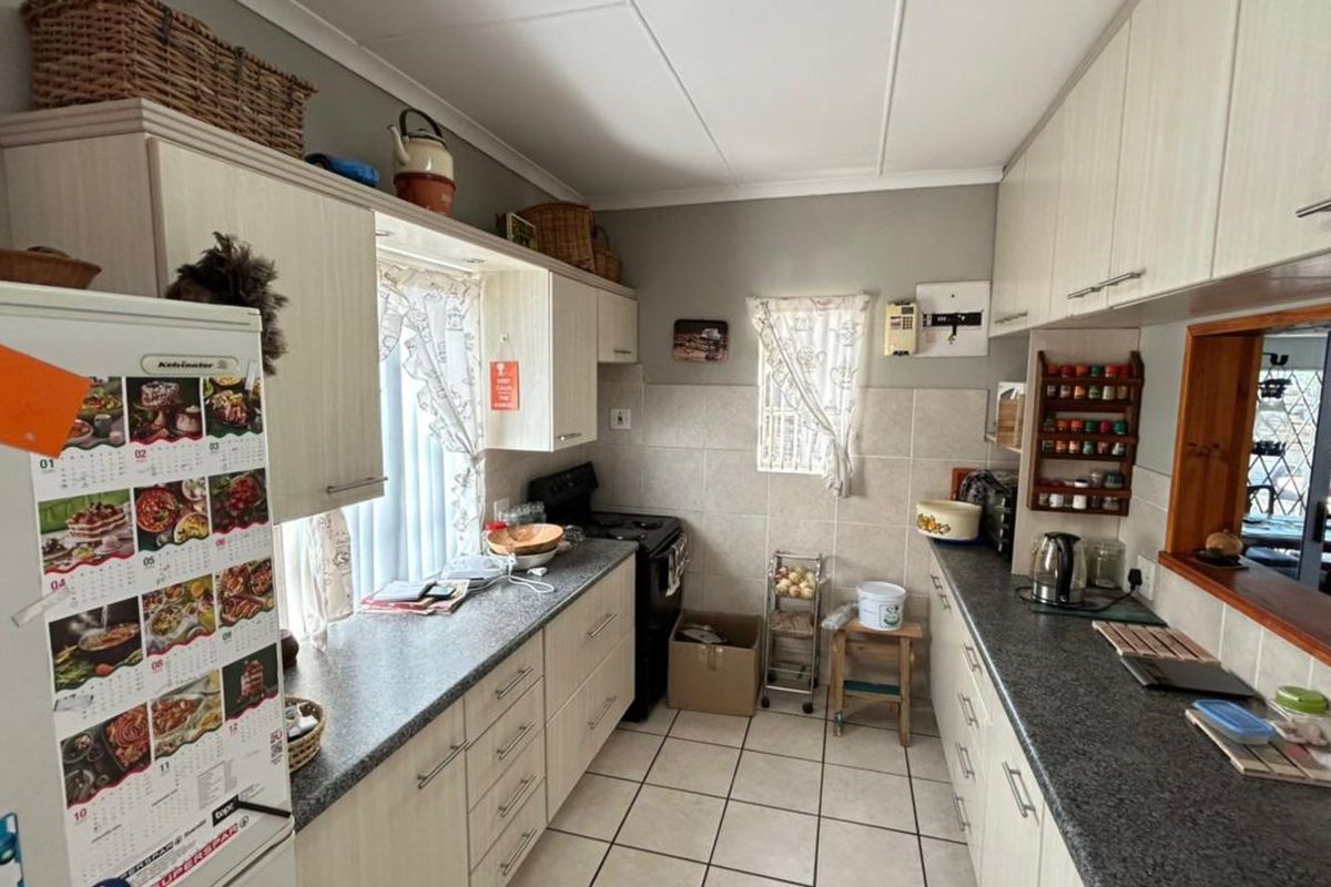 Functional galley-style kitchen featuring laminate countertops, tiled flooring, and ample built-in cabinetry with a pass-through window to the adjacent living area.