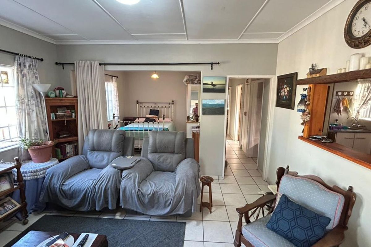 A living room area featuring tiled flooring and a ceiling with paneling, providing access to an adjacent bedroom and hallway.