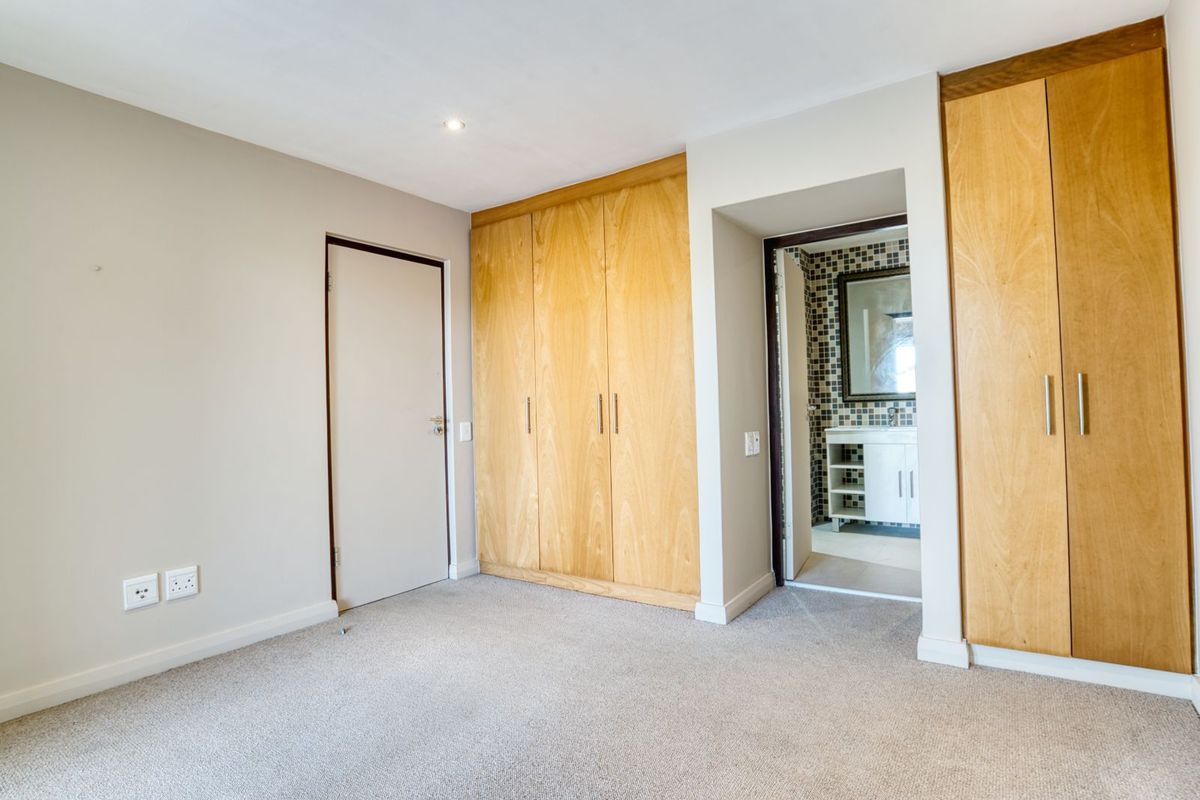 A well-maintained bedroom featuring built-in wooden cabinetry, neutral carpeting, and direct access to an en-suite bathroom with mosaic tile detailing.