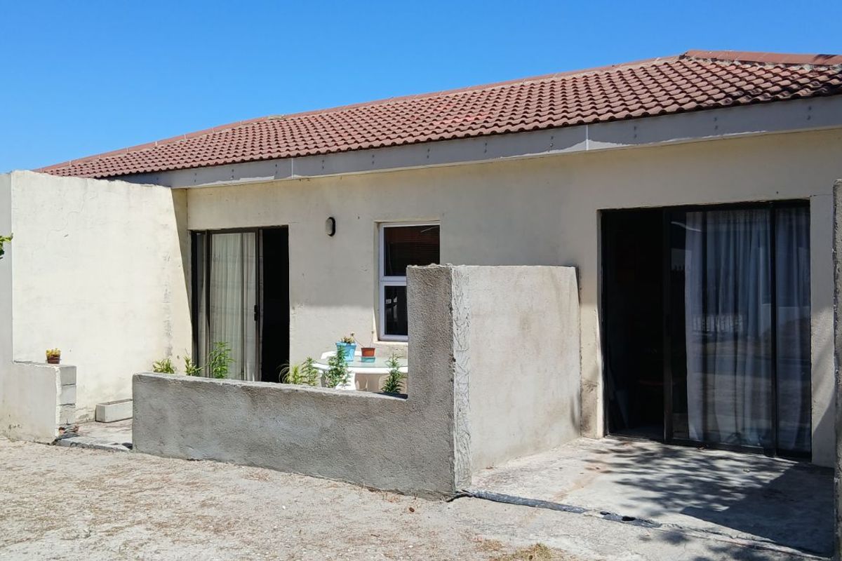 Rear view of a single-story house featuring a tiled roof, sliding glass doors, and an unfinished concrete patio wall.