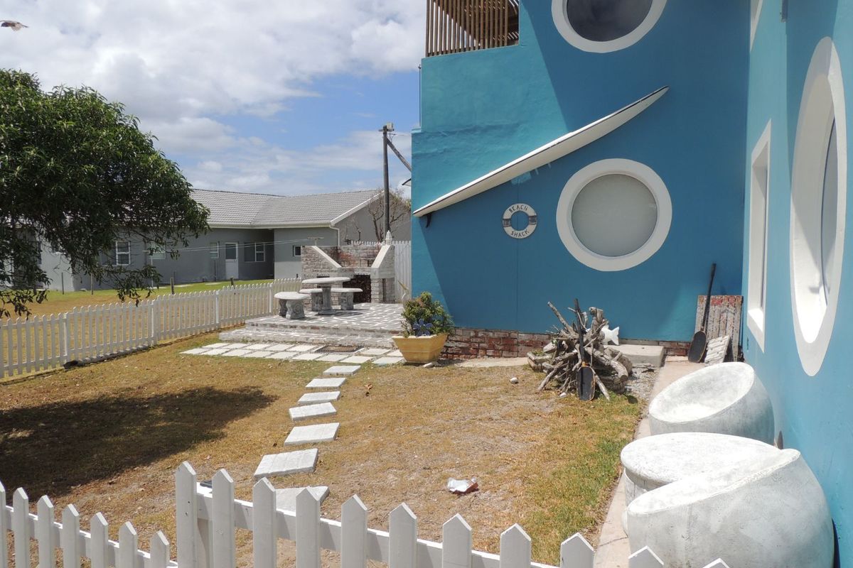 Rear garden area featuring a paved patio with a built-in brick braai, enclosed by a white picket fence.