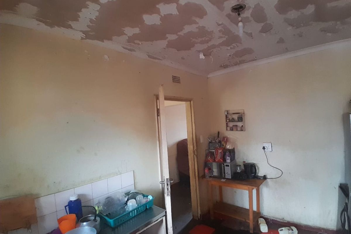A kitchen area requiring significant renovation, featuring damaged ceiling finishes, worn wall surfaces, and basic utility space.