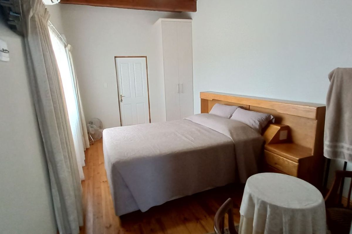 A bedroom featuring warm wooden flooring, a built-in wardrobe, and exposed timber ceiling beams.