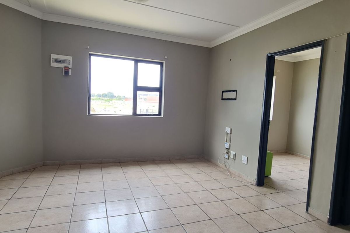 An empty bedroom featuring tiled flooring, neutral wall paint, and a window providing natural light, with an adjacent room visible through the doorway.