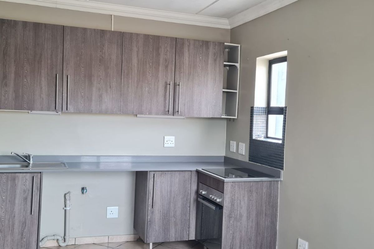 A functional kitchen featuring wood-grain cabinetry, a built-in oven and hob, and a stainless steel sink with tiled splashback.