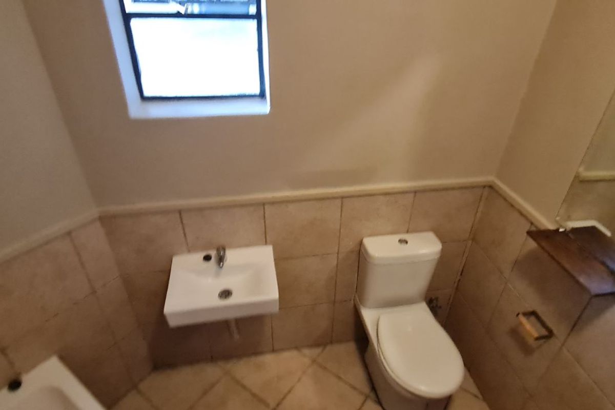 A compact bathroom featuring a wall-mounted basin, a standard toilet, and tiled walls with a neutral finish.