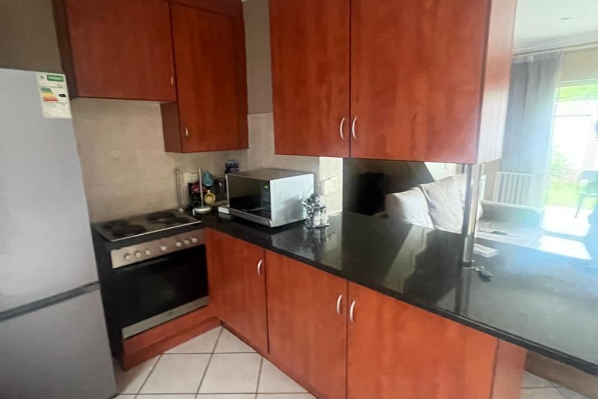 A functional kitchen featuring dark granite countertops, wood-finish cabinetry, a built-in oven and hob, and tiled flooring, opening into the adjacent living area.