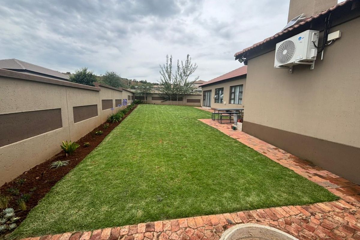 A well-maintained rear garden featuring a manicured lawn, paved walkway, and perimeter boundary wall with integrated air conditioning unit.