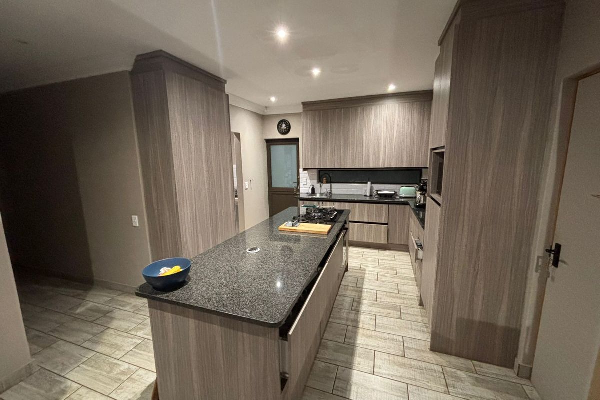 Modern kitchen featuring wood-grain cabinetry, a central island with a built-in gas hob, granite countertops, and tiled flooring.
