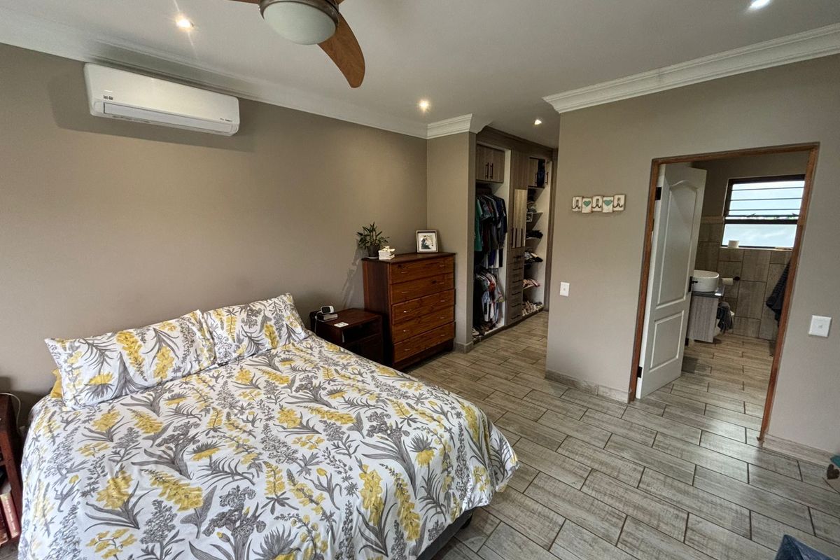 Spacious bedroom featuring tiled flooring, a ceiling fan, wall-mounted air conditioning unit, and an integrated walk-in closet leading to an en-suite bathroom.