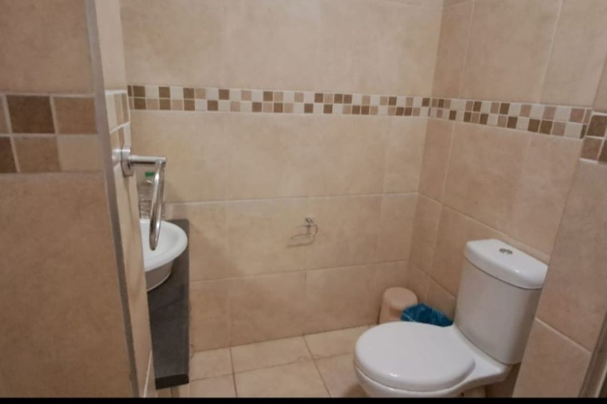 A compact bathroom featuring neutral wall tiles with a decorative mosaic border, a standard toilet, and a small vanity basin.