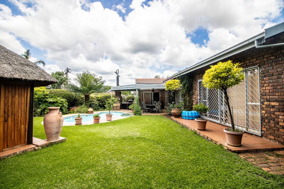 A spacious rear garden featuring a swimming pool, a thatched lapa, and a paved patio area adjacent to the main house.