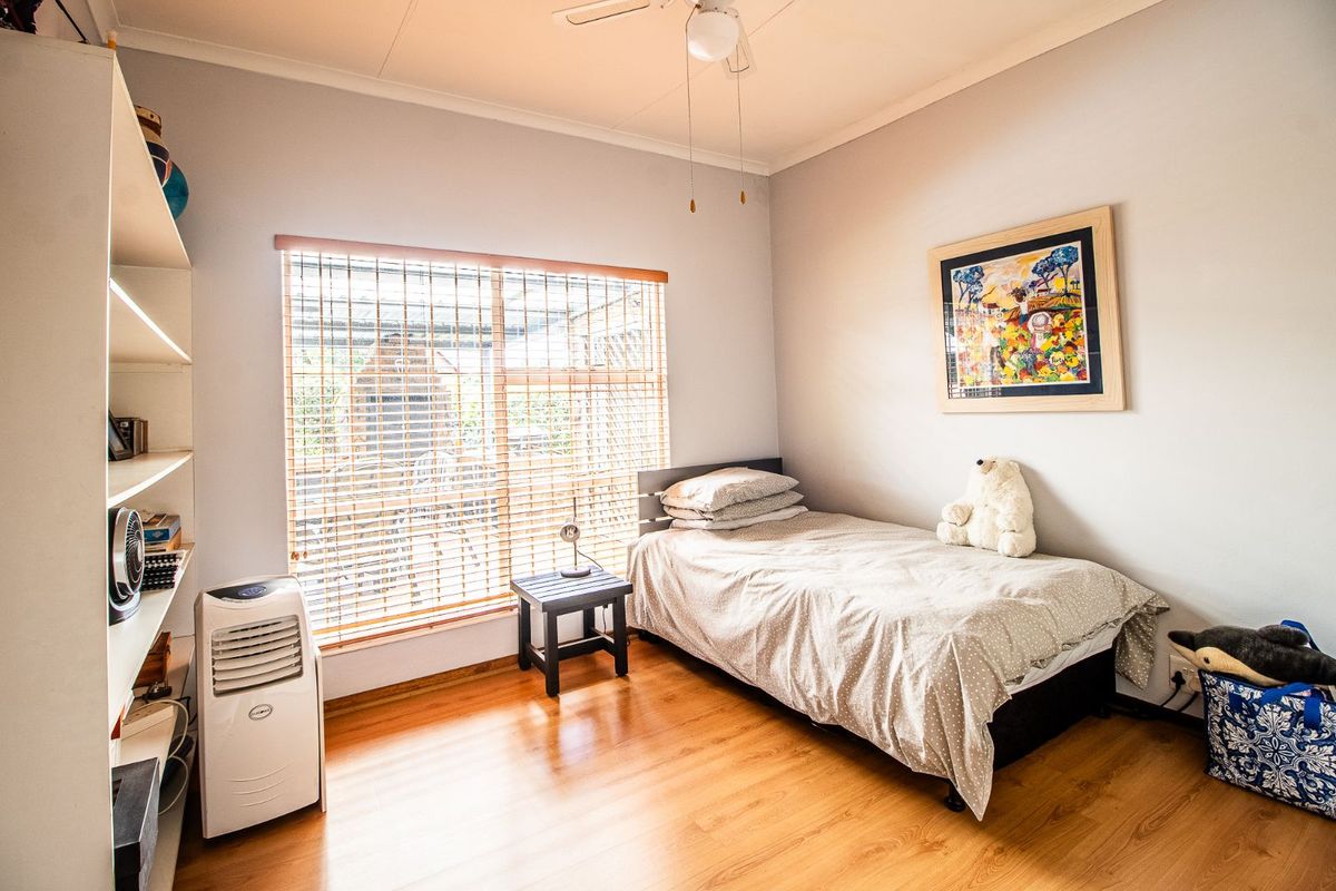 A well-lit bedroom featuring laminate flooring, a ceiling fan, and large windows with fitted blinds, offering a comfortable and functional living space.