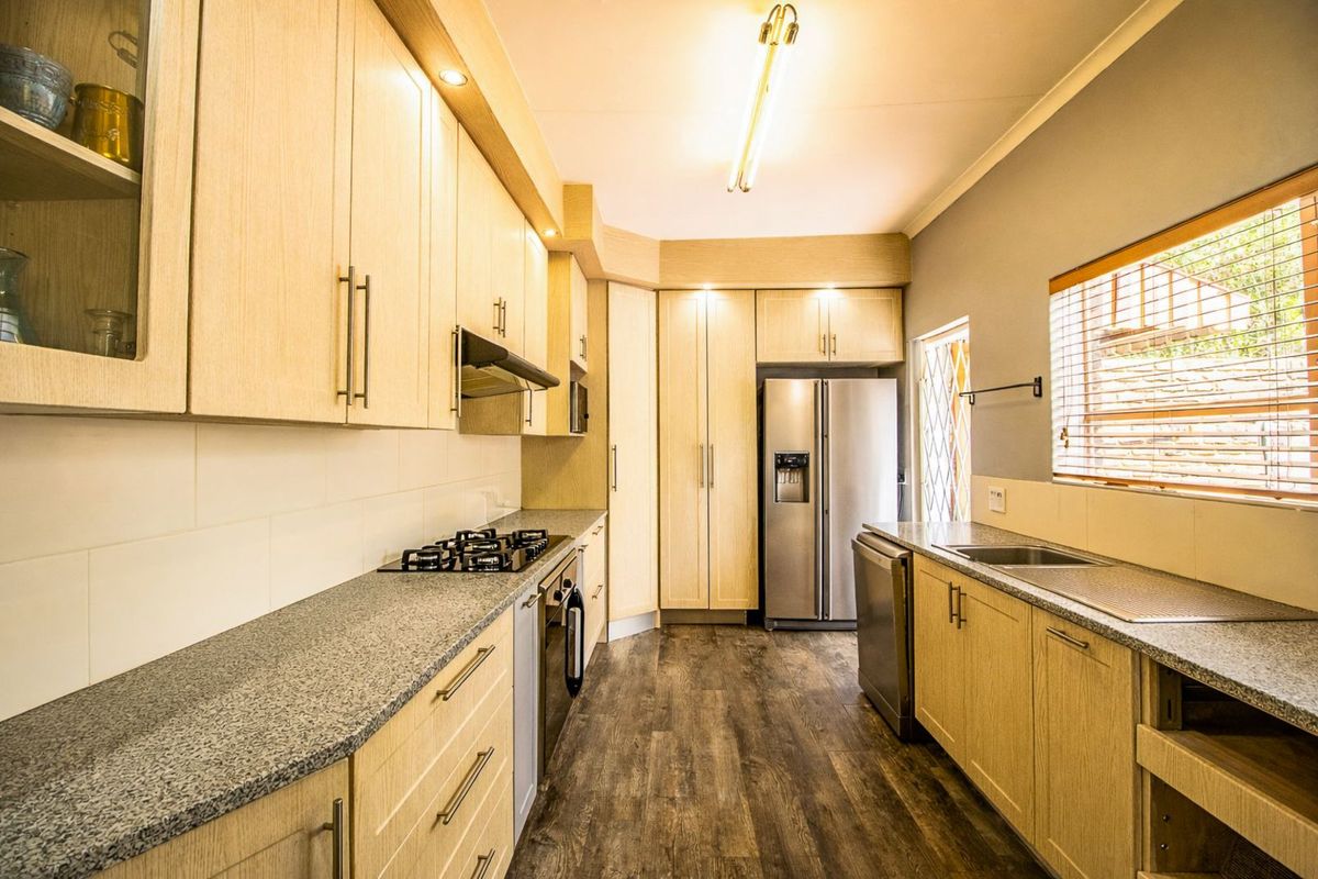 A functional kitchen featuring light wood cabinetry, granite countertops, a built-in gas hob, and wood-look flooring.