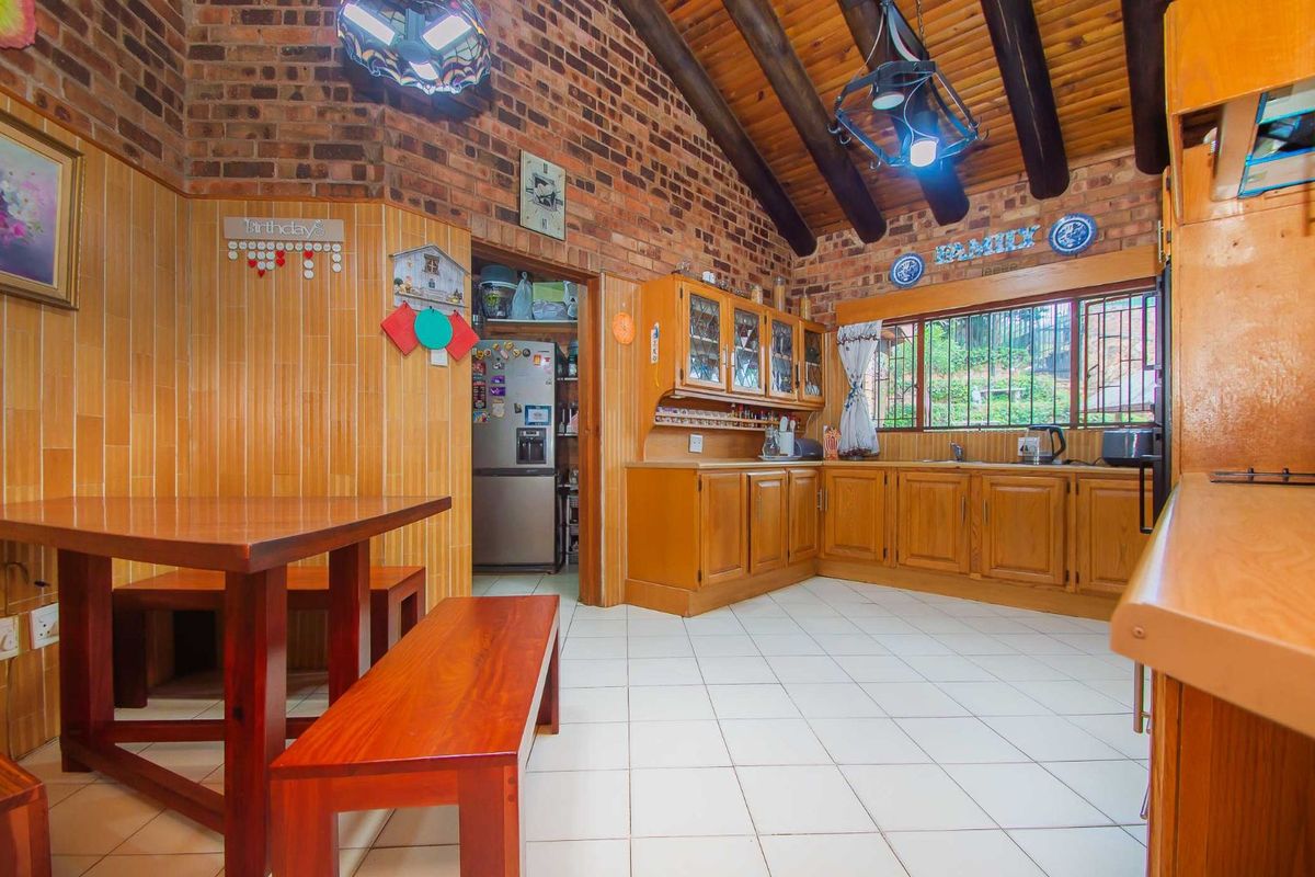 A rustic kitchen featuring exposed brick walls, timber ceiling beams, wooden cabinetry, and tiled flooring, with an adjacent pantry area.