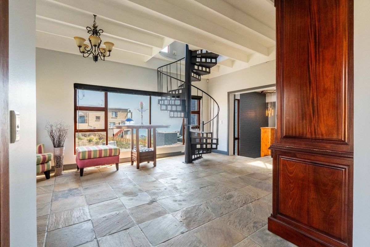 Spacious living area featuring natural stone flooring, exposed beam ceiling, and a striking black metal spiral staircase leading to the upper level.