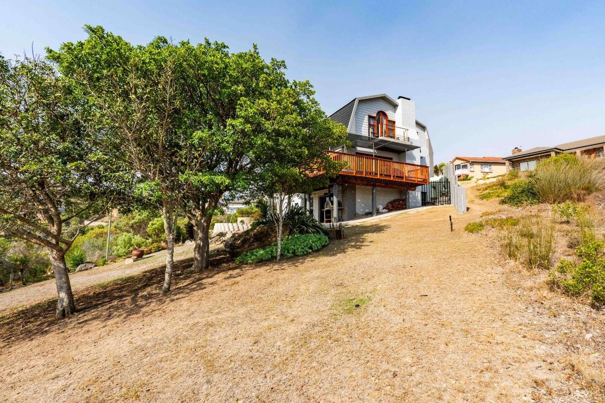 Rear view of a multi-level house featuring a raised wooden deck, balcony, and sloped garden area.