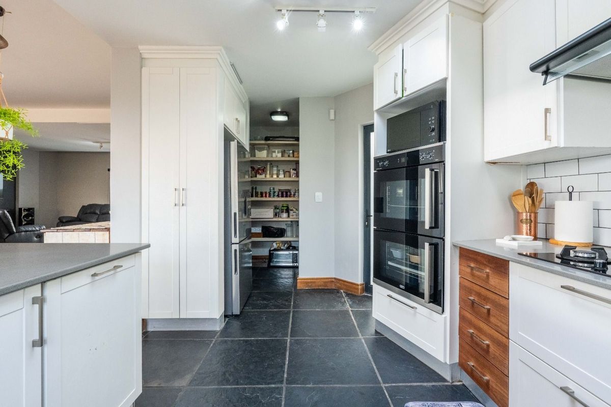 Modern kitchen featuring built-in double ovens, integrated microwave, stone countertops, and a convenient walk-in pantry with shelving.